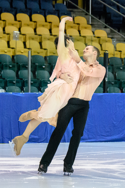 A man holds a woman by her waist near his hip. They smile at one another.